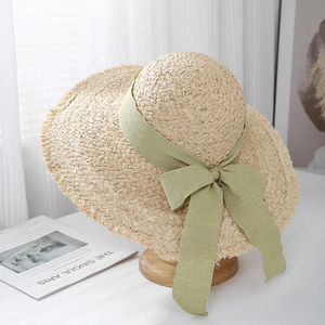 Detail of raffia straw sun hat featuring a wide frayed brim and sage green ribbon bow