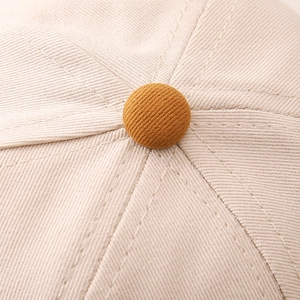 Close-up of the beige cotton twill baseball cap top with a mustard yellow button detail