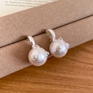 Elegant silver C-shaped pearl stud earrings with zircon stars on brown velvet stand