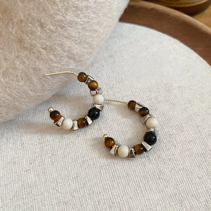 Macro detail of C-shape tiger eye stone earrings on beige linen with golden studs