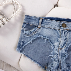 Dettaglio macro degli shorts di jeans blu a vita alta con orli sfrangiati e bottone metallico