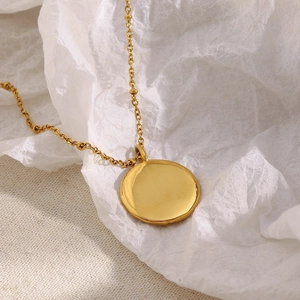 Détail d'une chaîne à billes en acier doré 18K avec un pendentif pièce ronde polie
