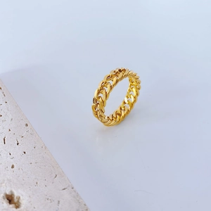 Close-up of a polished 18k gold curb chain ring on a minimalist white stone background