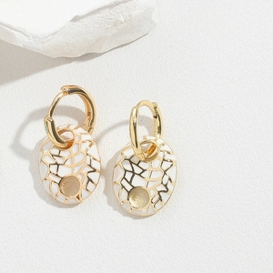 Macro detail of oval gold-tone earrings with white enamel and golden geometric grid