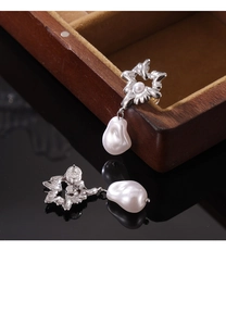Close-up of vintage irregular floral metal earrings with baroque pearl drops on a black mirror