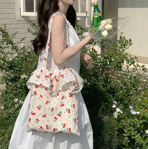Detail of white canvas tote bag with cherry print and elegant ruffle trim