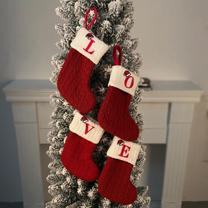 Close-up of four red and white knitted Christmas stockings spelling LOVE on a snowy tree
