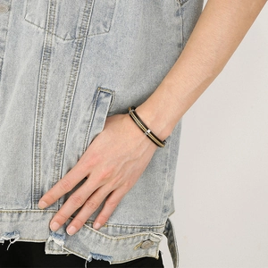 Detail of men's leather bracelet with gold chain inlay worn against denim vest
