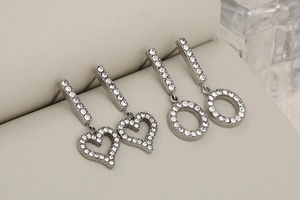 Macro detail of silver-tone rhinestone earrings featuring heart and round pendant designs