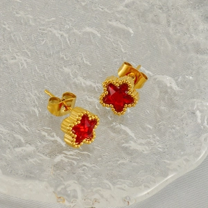 Goldene Stern-Ohrstecker mit rotem Stein und Perlenbesatz auf strukturiertem Glastablett
