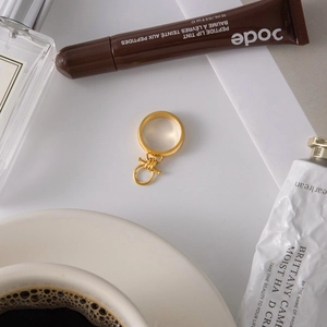 Flat lay of a gold toggle clasp ring with elegant lifestyle accessories on a clean surface