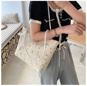 Straw tote bag featuring floral embroidery and lace bow detail worn by a model
