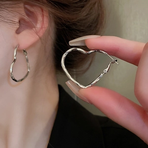 Close-up of heart-shaped silver earrings with model shot showing the fit and size