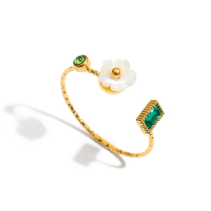 Detail of adjustable gold ring featuring white shell flower and green gemstone accents