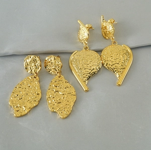 Detailed view of gold plated leaf earrings with vintage hammered texture on gray fabric
