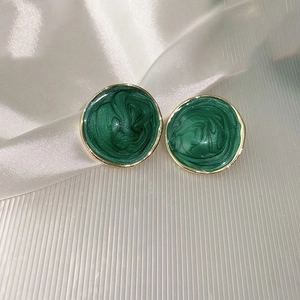 Macro shot of green enamel stud earrings with gold frames on white silk fabric