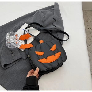 Detail of a black pumpkin crossbody bag with orange face and cute bat charms on the strap