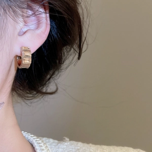 Detailed close-up of golden C-shaped earring with three step-cut cubic zirconia stones