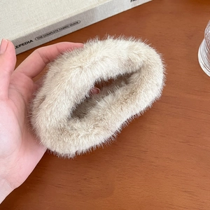 Détail d'une pince à cheveux en fausse fourrure beige tenue sur fond de table en bois
