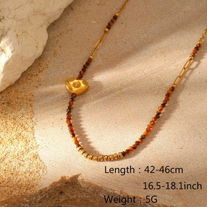 Detail of layered beaded necklace with tiger eye stones and gold heart pendant on sand