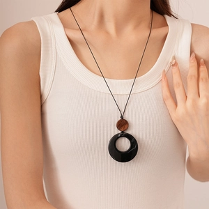 Minimalist resin and wood pendant necklace on long black cord worn with white vest