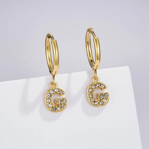 Close-up of golden letter G pendant with sparkling cubic zirconia on stainless steel earring