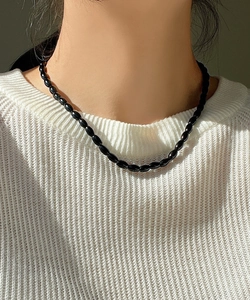 Minimalist black onyx oval bead necklace worn over a white knit sweater with soft natural light