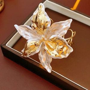 Macro shot of lily flower cuff bangle with gold and white enamel petals in a gift box