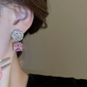 Macro view of silver flower earrings with square pink gemstone pendant on ear