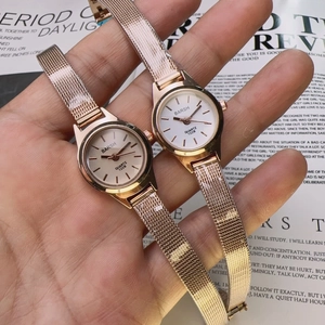 Detail of two golden mesh strap watches with white dials on a text-filled background