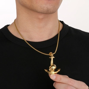 Detailansicht goldener Anker- und Totenkopfanhänger getragen auf schwarzem T-Shirt