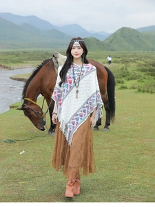 Ethnic style white knit shawl with colorful patterns and fringe on a grassy landscape