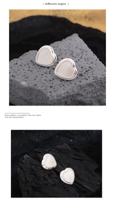 Detail of silver heart earrings with white shell inlay on textured volcanic stone