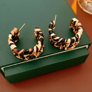 Detail of C-shaped leopard print earrings with woven texture on a green jewelry box