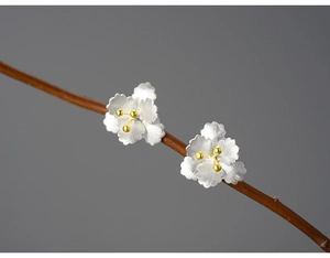 Macro view of silver begonia earrings with gold centers on a rustic branch