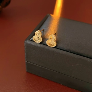 Macro shot of gold-plated gourd earrings with textured facets on a jewelry box