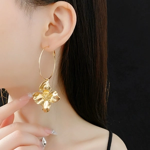 Detailed view of large gold floral pendant earrings with a minimalist metallic ring design