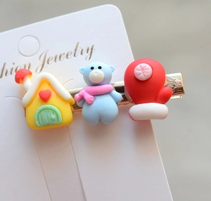 Close-up of festive hair clips featuring resin bear, heart house and red glove charms
