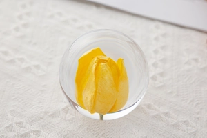 Detailed view of a yellow tulip crystal ball ornament on white lace texture fabric