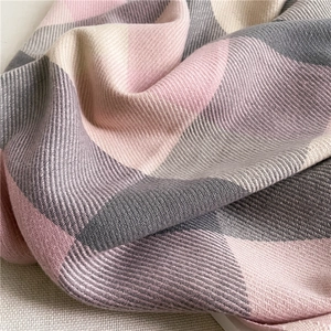 Close-up of soft plaid scarf fabric showing pink and grey woven textures and patterns