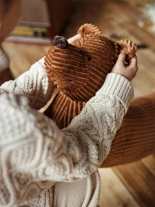 Détail d'une peluche en velours côtelé marron tenue par un enfant en pull à torsades