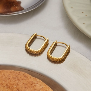 Detailed view of gold U-shaped earrings with bubble texture on a metal tray