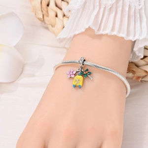 Detail of travel charms featuring a pink flower, yellow suitcase, and palm tree on a bracelet