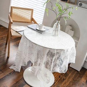 Elegant white lace tablecloth with hollow embroidery on a round coffee table in a room