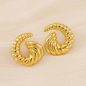 Détail macro de boucles d'oreilles spirales plaquées or sur fond de soie beige
