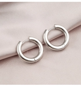 Close-up of polished silver hoop earrings on soft pink silk fabric texture