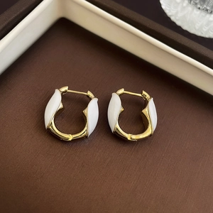 Macro shot of U-shaped gold enamel earrings inside a textured brown jewelry box
