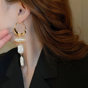 Close-up of elegant gold drop earrings with baroque pearls worn by a model