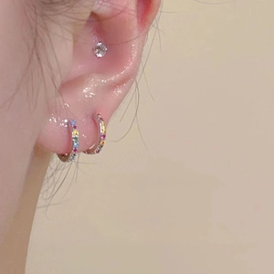 Detail of colorful rainbow zircon hoop earrings and single stud on a model's ear