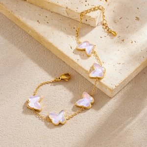 Gold butterfly charm bracelet with five white pearlescent pendants on stone background